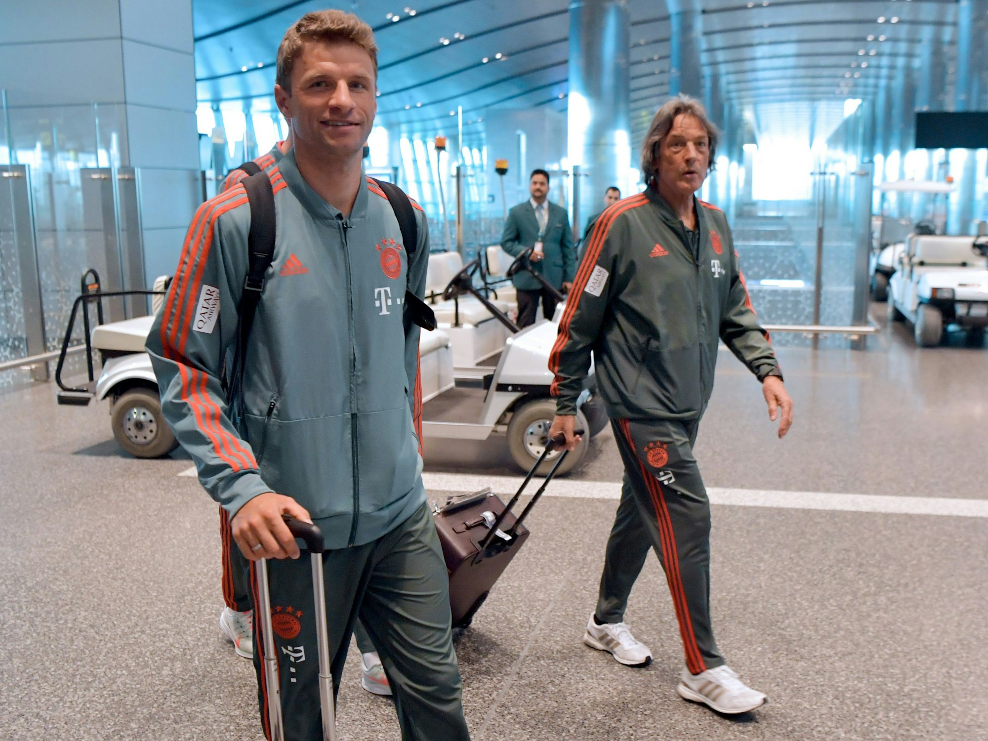 Thomas Müller vom FC Bayern München läuft im Flughafenterminal Doha über den Gang des Gebäudes. Rechts geht Vereinsarzt Hans-Wilhelm Müller-Wohlfahrt.
