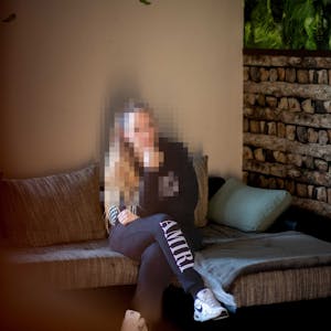 Das Bild zeigt Nadine Schäfer, wie sie auf einem Sofa sitzt. Ihr Gesicht ist zu ihrem Schutz gepixelt.