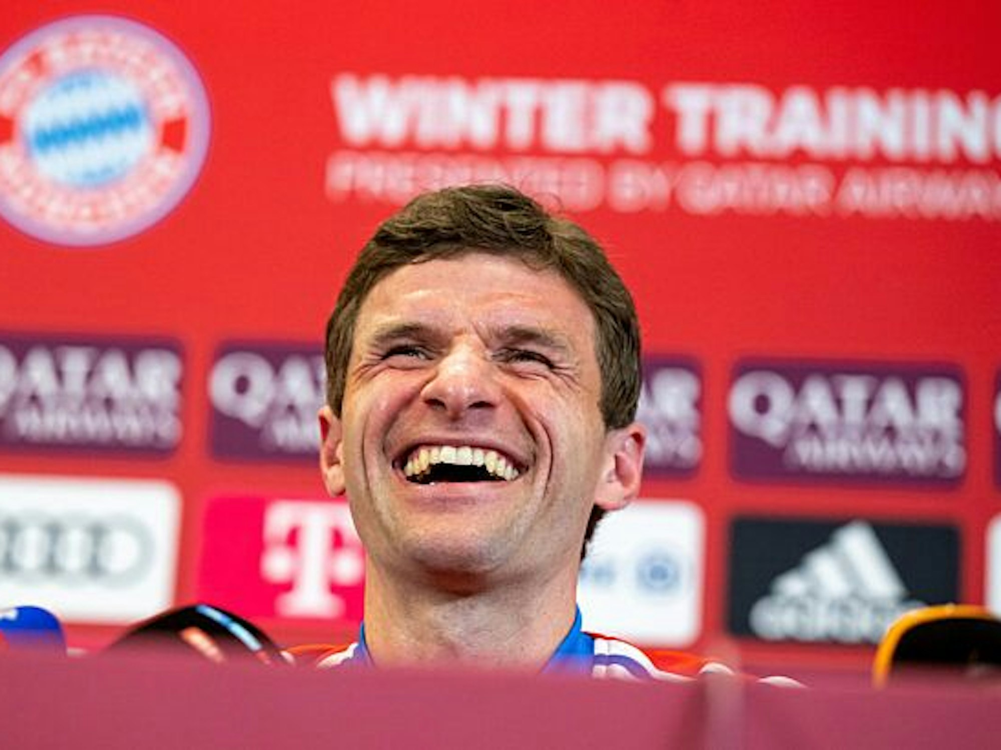 Thomas Müller nimmt an einer Pressekonferenz des FC Bayern München teil und lacht.