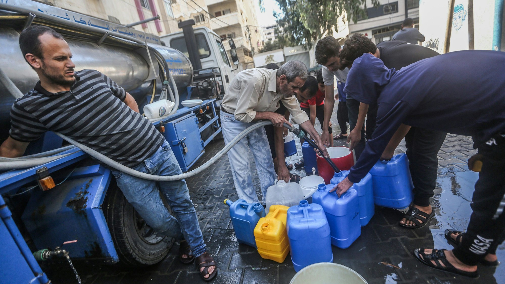 Palästinenser füllen in Gaza City Behälter mit Trinkwasser aus einem Wasserverteilungsfahrzeug auf.