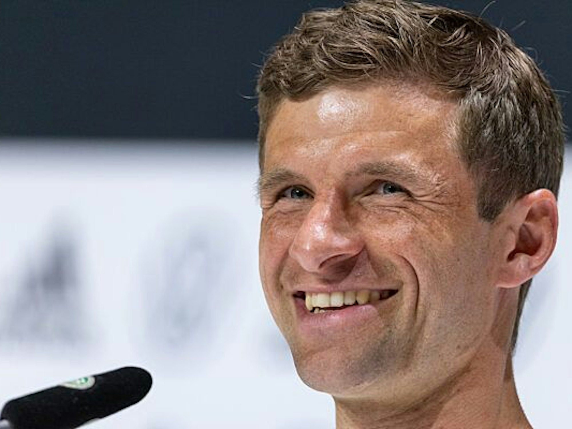 Der Spieler Thomas Müller nimmt an einer Pressekonferenz teil. Er lächelt herzlich.