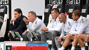 Gerardo Seoane und sein Trainerteam sitzen beim Test-Spiel von Borussia Mönchengladbach gegen den HSC Montpellier auf der Trainerbank und beobachten das Spiel.