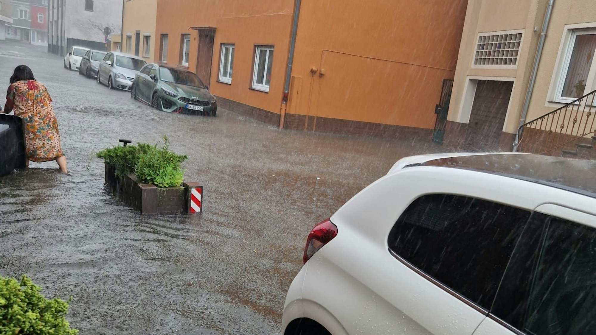 Eine Frau watet durch eine überflutete Straße, Autos stehen im Wasser.