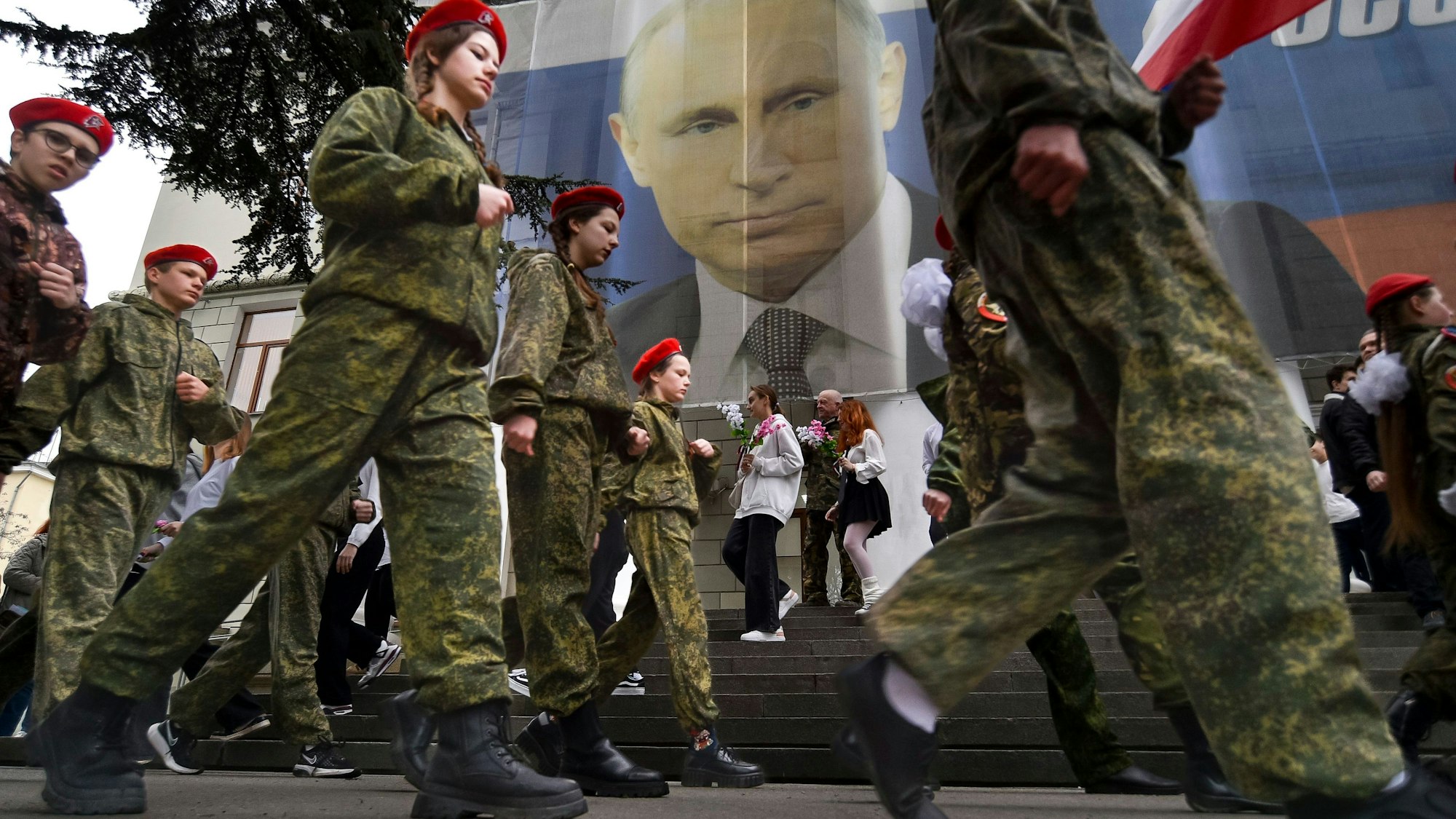 17. März 2023: Uniformierte Jugendliche marschieren in Jalta anlässlich einer Aktion zum neunten Jahrestag der Krim-Annexion an einem Bildnis des russischen Präsidenten Wladimir Putin (im Hintergrund) vorbei. Foto: U