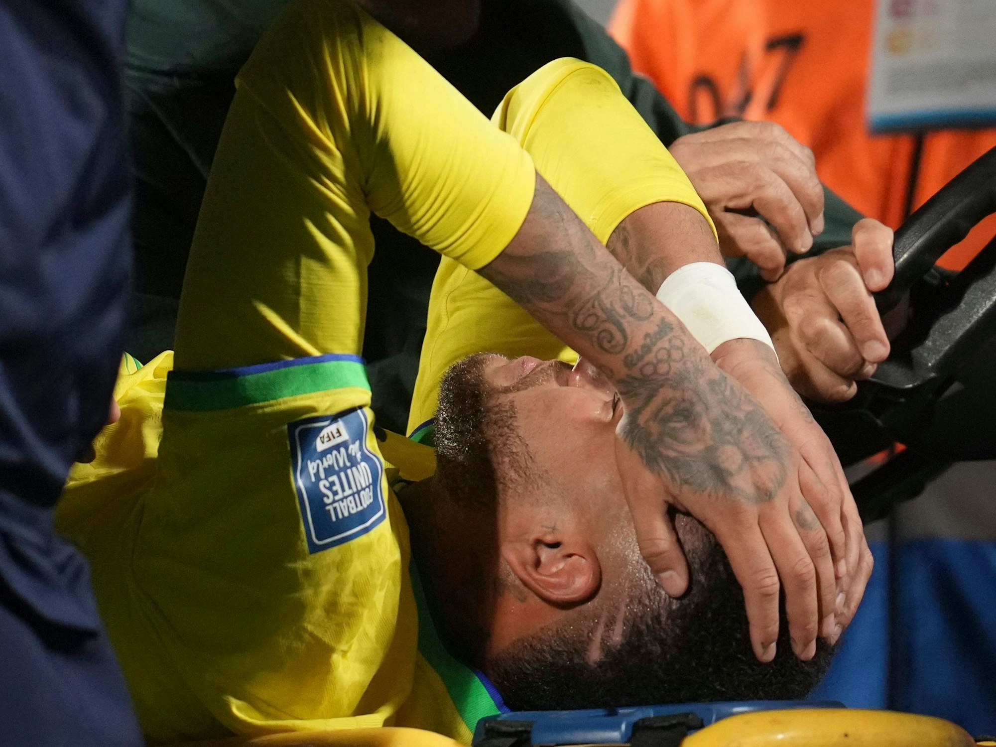 Neymar wird verletzt vom Platz gebracht. Er hält sich mit beiden Händen das Gesicht.