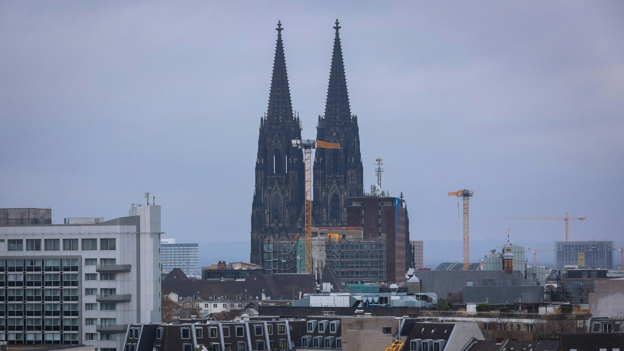 Der Kölner Dom vor einem bedeckten Himmel mit Kran im Vordergrund.