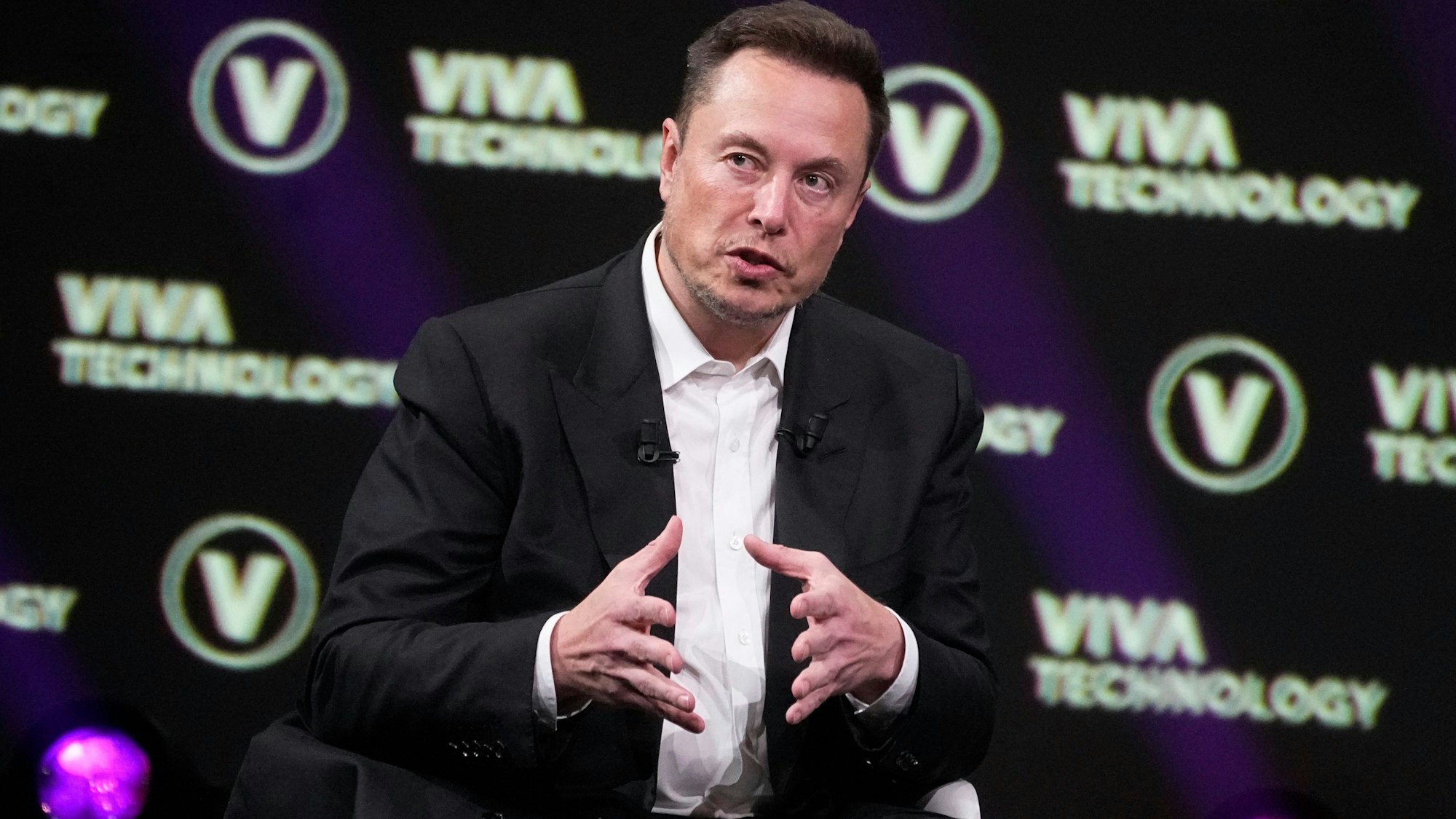 Elon Musk im Anzug und Hemd vor einer Leinwand mit der Aufschrift "Viva Technology"