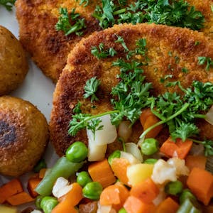 Falafel, vegane Schnitzel und Gemüse liegen garniert mit Petersilie auf einem Teller.