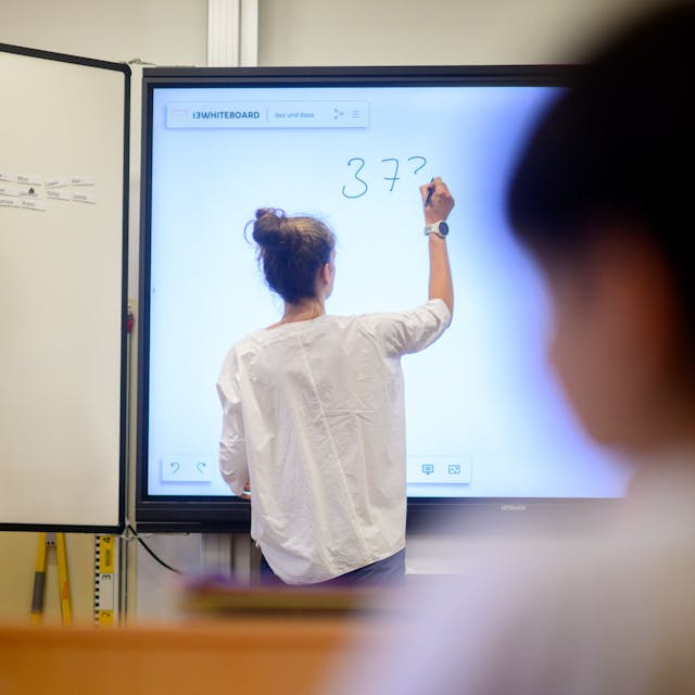 Eine Lehrerin steht mit dem Rücken zur Klasse an einer digitalen Tafel.