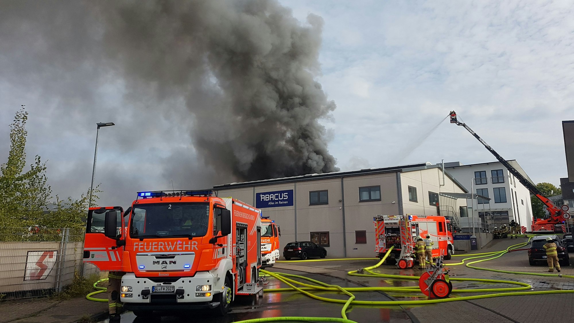 Ein Feuerwehrauto steht vor einem Gebäude: Schwarzer Rauch steigt über der Chemiefabrik in Bergisch Gladbach-Frankenforst auf.