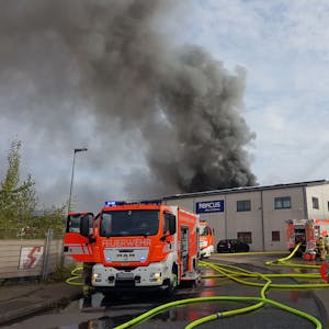 Ein Feuerwehrauto steht vor einem Gebäude: Schwarzer Rauch steigt über der Chemiefabrik in Bergisch Gladbach-Frankenforst auf.