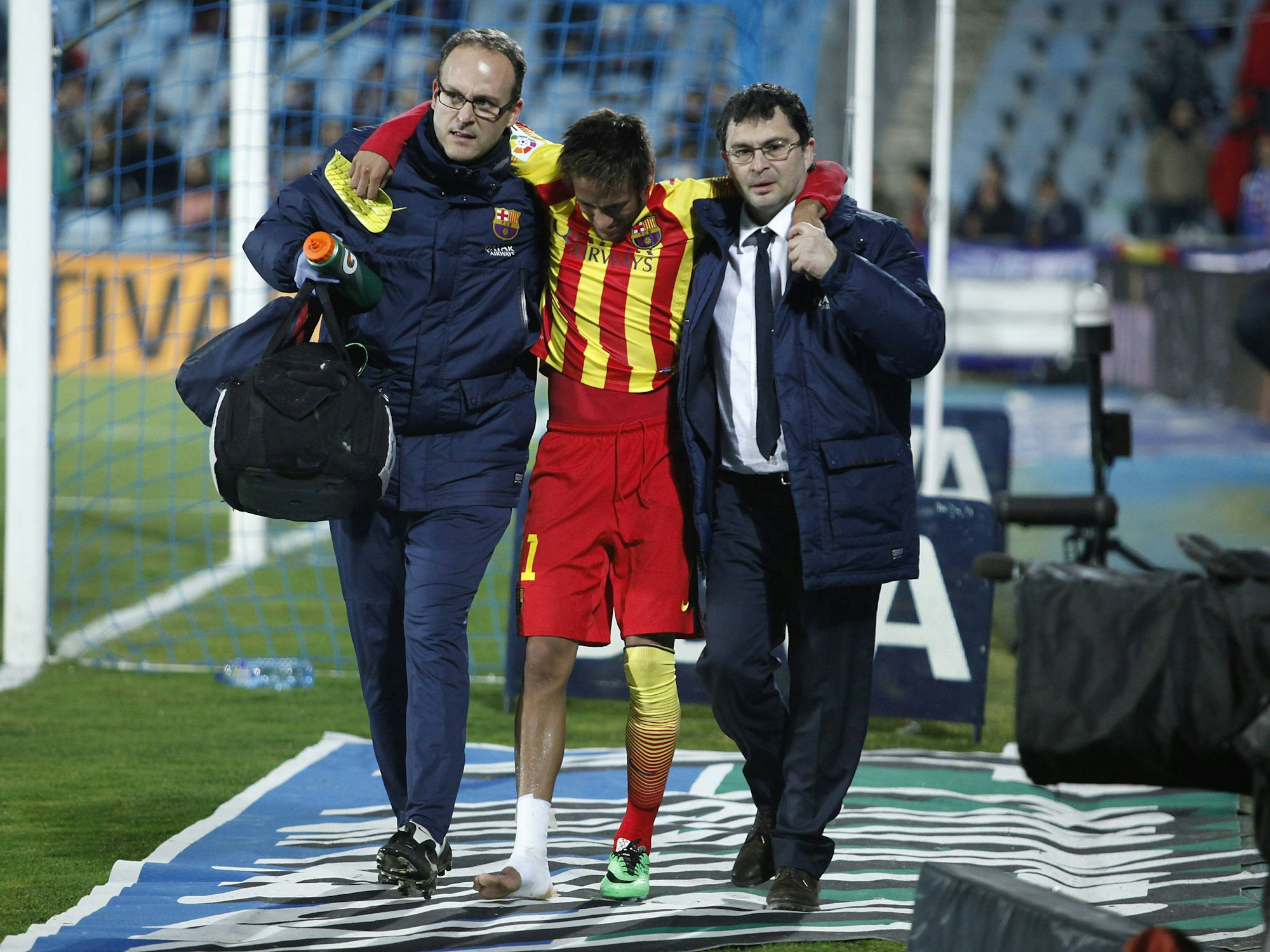 Neymar wird von zwei Mitarbeitern des FC Barcelona am Seitenrand Richtung Kabine gestützt. Sein Knöchel ist mit Verband umwickelt.