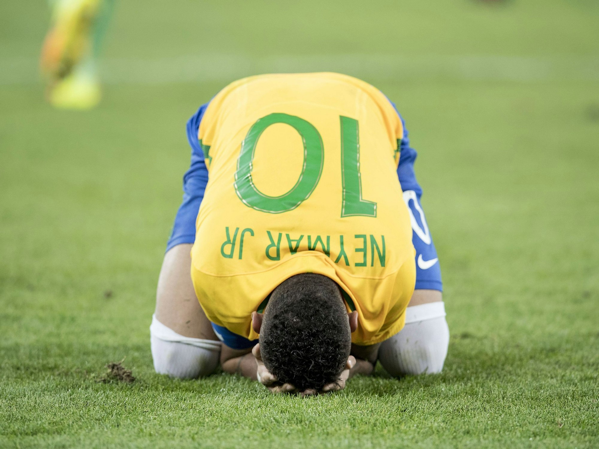 Mittig im Bild kniet Neymar Jr. im Trikot der Brasilianischen Selecao mit der Nummer 10 und legt seinen Kopf auf den Boden. Er hat das Gesicht in seinen Händen vergraben.