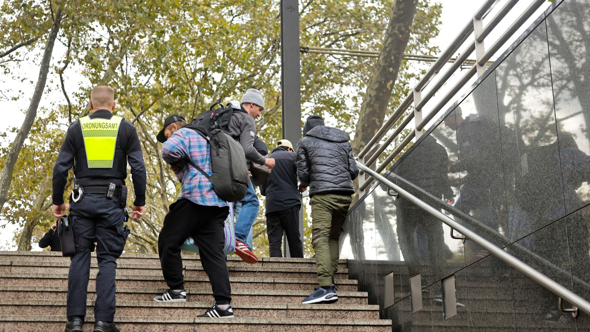 Das Bild zeigt einen Mitarbeiter der Stadt, der auf einer Treppe am Neumarkt Menschen kontrolliert.