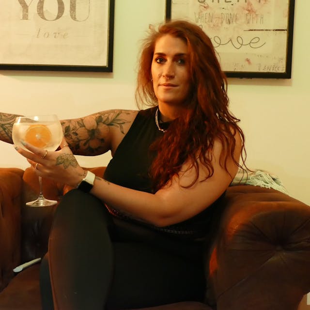 Eine Frau sitzt auf einem Sessel und hält ein Glas mit einem Getränk in der Hand.