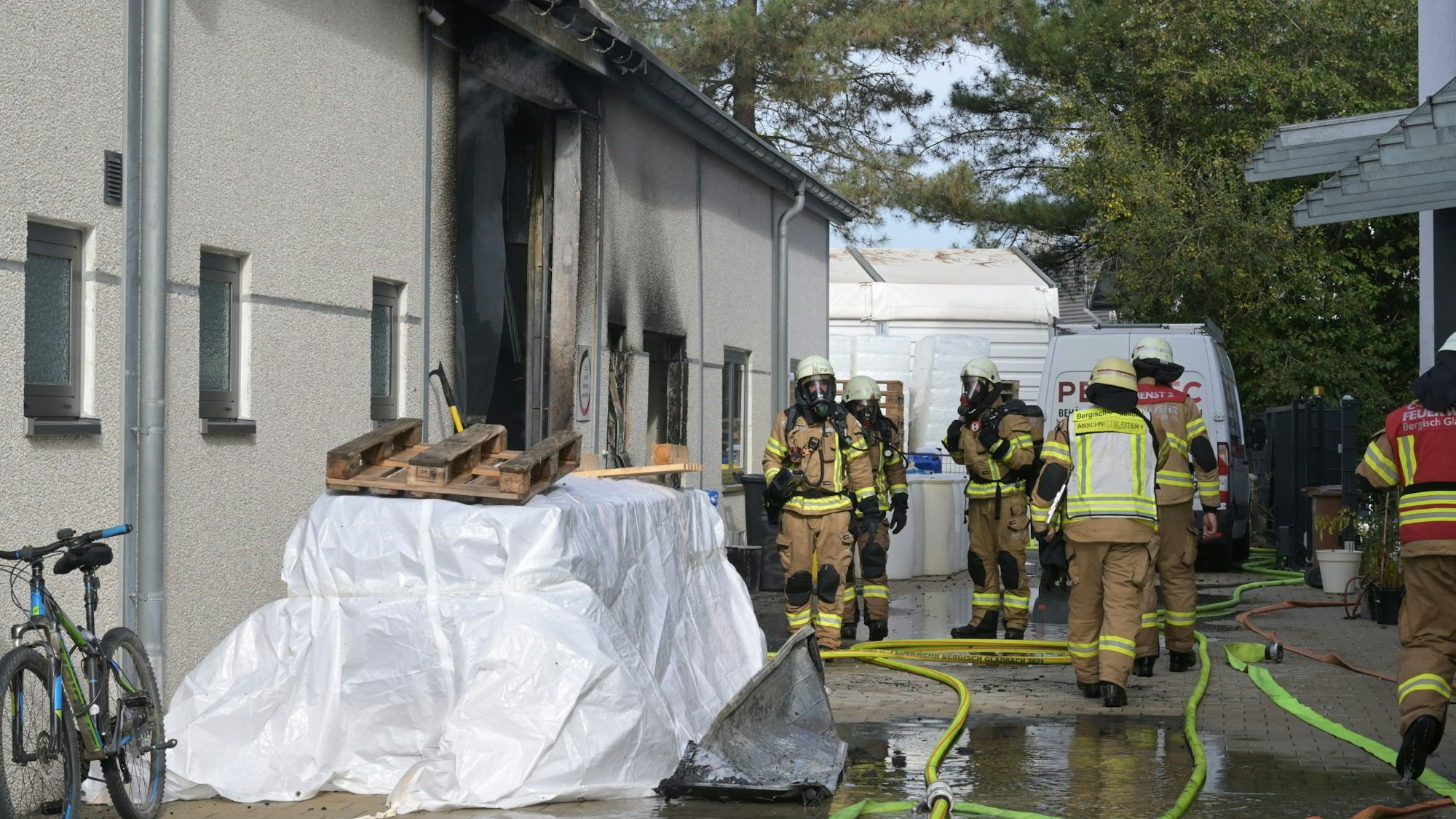 Feuerwehrleute mit Atemschutzausrüstung stehen am Eingang einer verrußten Gewerbehalle.
