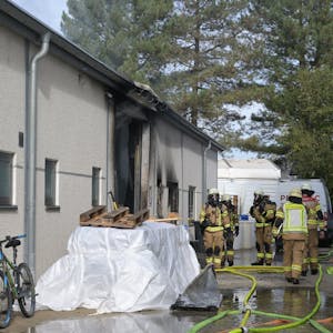 Feuerwehrleute mit Atemschutzausrüstung stehen am Eingang einer verrußten Gewerbehalle.
