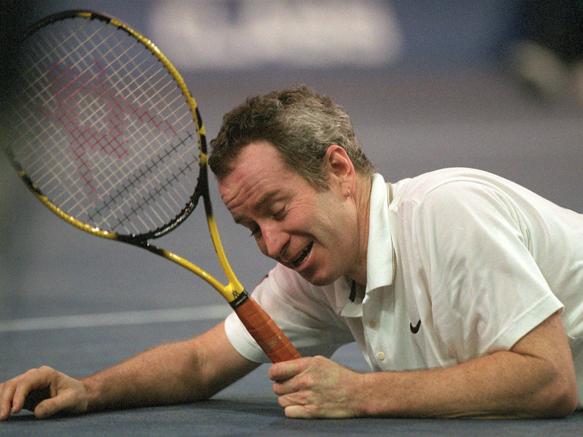 Mit dem Tennisschläger in der Hand liegt der Amerikaner John McEnroe am Boden und lächelt gequält.