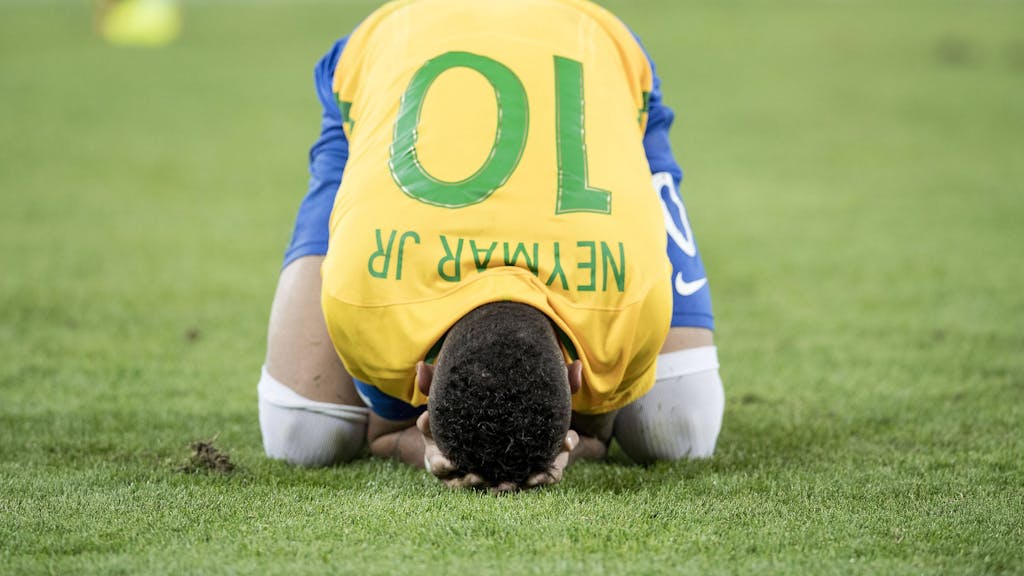 Mittig im Bild kniet Neymar Jr. im Trikot der Brasilianischen Selecao mit der Nummer 10 und legt seinen Kopf auf den Boden. Er hat das Gesicht in seinen Händen vergraben.