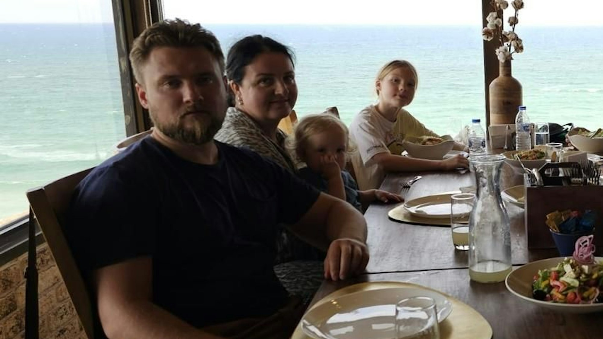 Die Familie sitzt in einem Restaurant mit Meerblick.