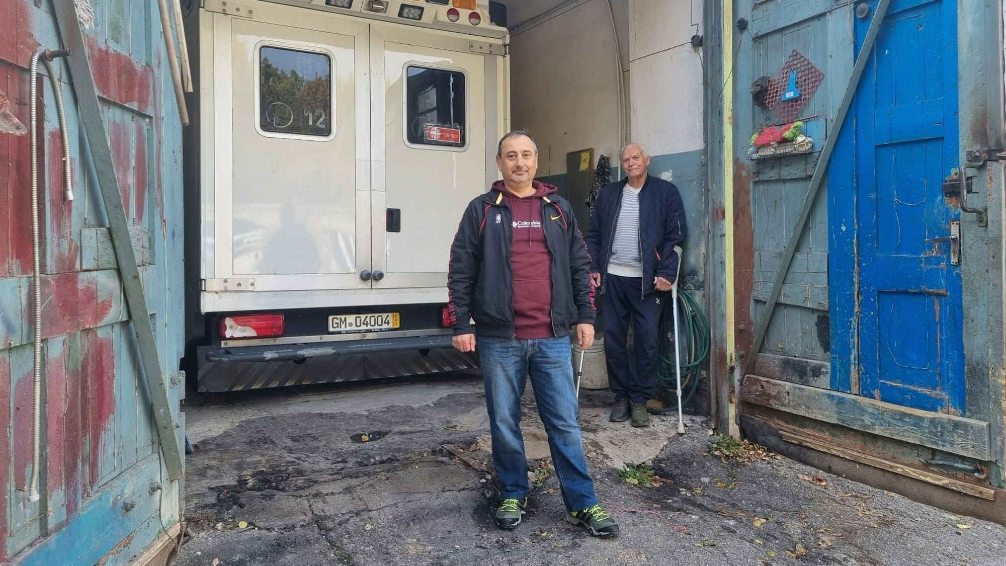Igor Prudkov steht neben einem alten Krankenwagen. Hinter ihm steht ein Mann mit Gehhilfen.