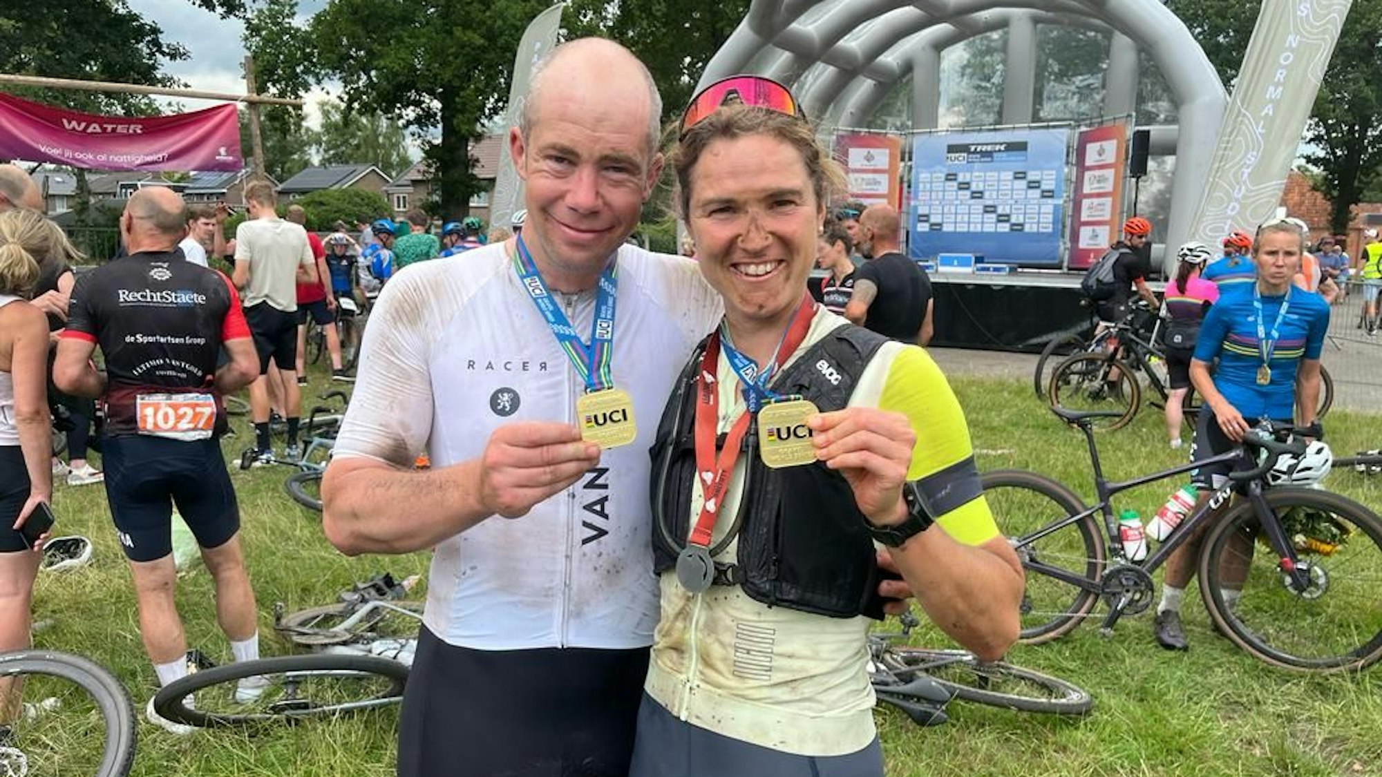 Ein Mann und eine Frau halten Medaillen in der Hand. Im Hintergrund liegen Fahrräder auf der Wiese.