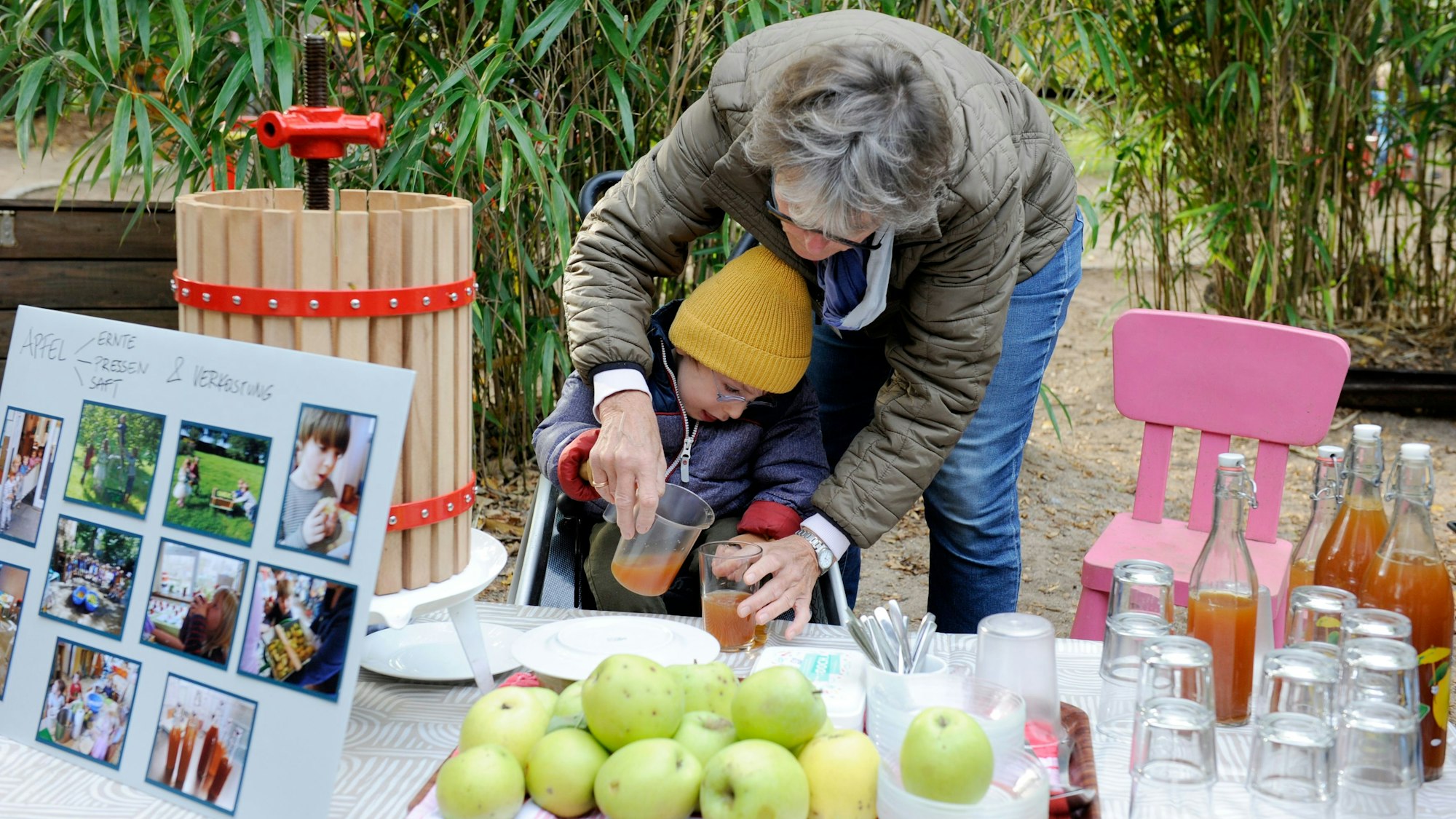 Ein Junge und eine Erzieherin schenken in der Klimakita Düsseldorf selbstgepressten Apfelsaft aus.