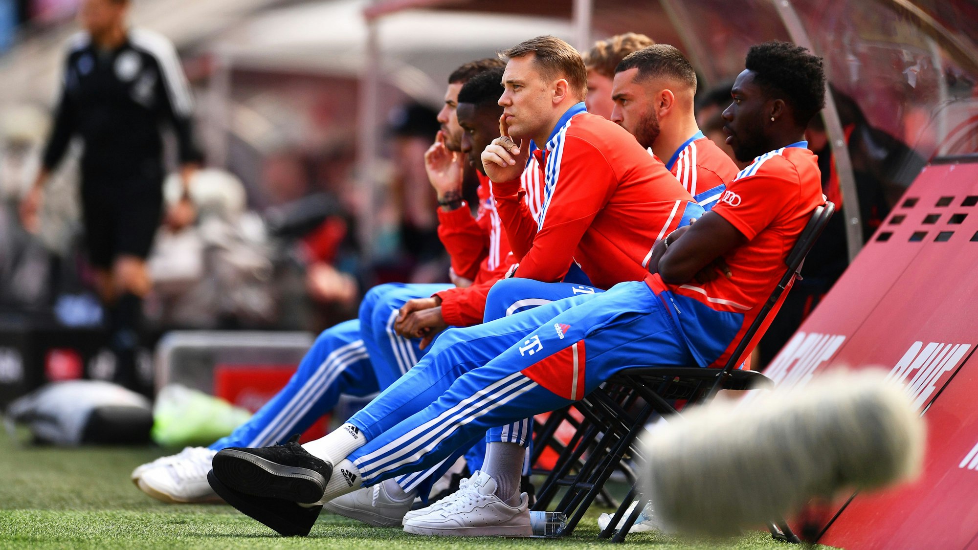 Bayerns Torhüter Manuel Neuer (M) sitzt neben einigen Teamkollegen auf Klappstühlen neben der Spielerbank.