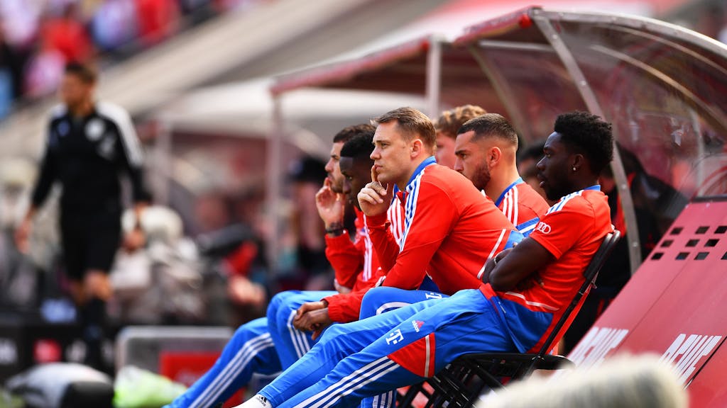 Bayerns Torhüter Manuel Neuer (M) sitzt neben einigen Teamkollegen auf Klappstühlen neben der Spielerbank.