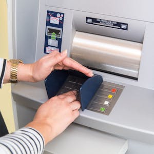 Eine Person gibt die Geheimzahl ihrer Zahlungskarte an einem Geldautomaten ein.