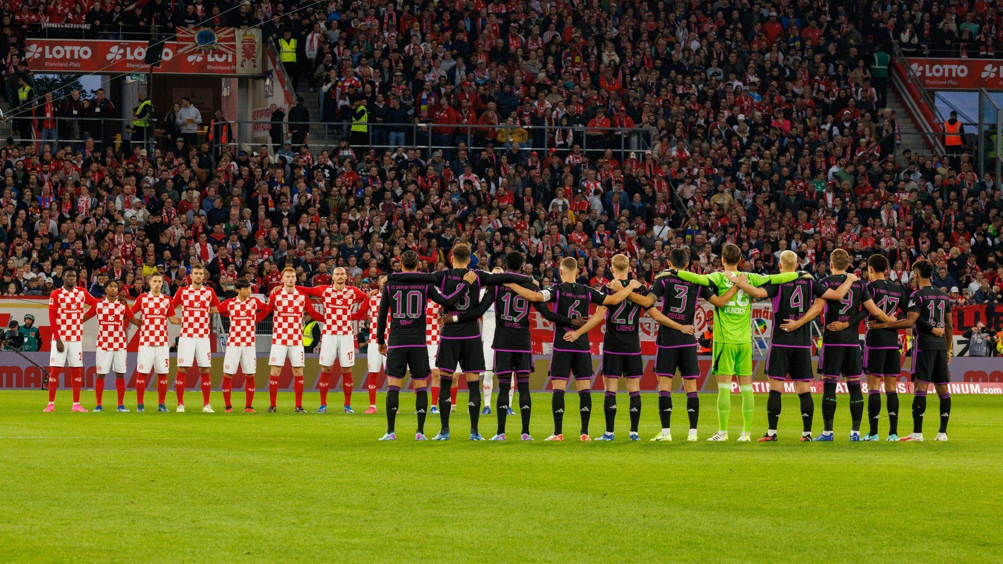 Spieler von Bayern München und dem FSV Mainz 05 stehen bei einer Schweigeminute Arm in Arm mit ihren Mitspielern.