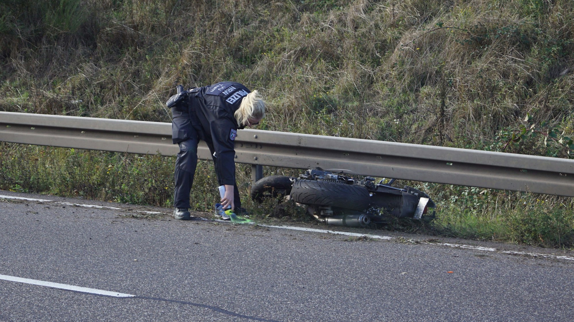 Eine Polizistin markiert Spuren nach einem Unfall, bei dem ein Motorradfahrer auf der B266 bei Mechernich-Firmenich ums Leben gekommen ist. Das Motorrad liegt an einer Leitplanke.