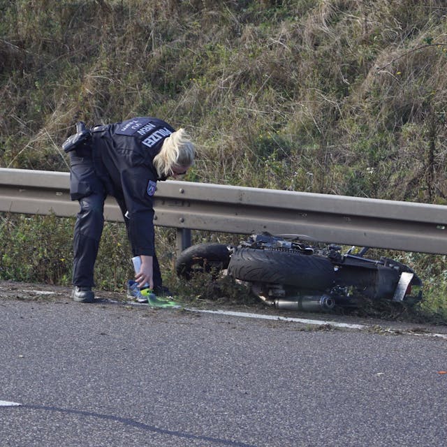 Eine Polizistin markiert Spuren nach einem Unfall, bei dem ein Motorradfahrer auf der B266 bei Mechernich-Firmenich ums Leben gekommen ist. Das Motorrad liegt an einer Leitplanke.