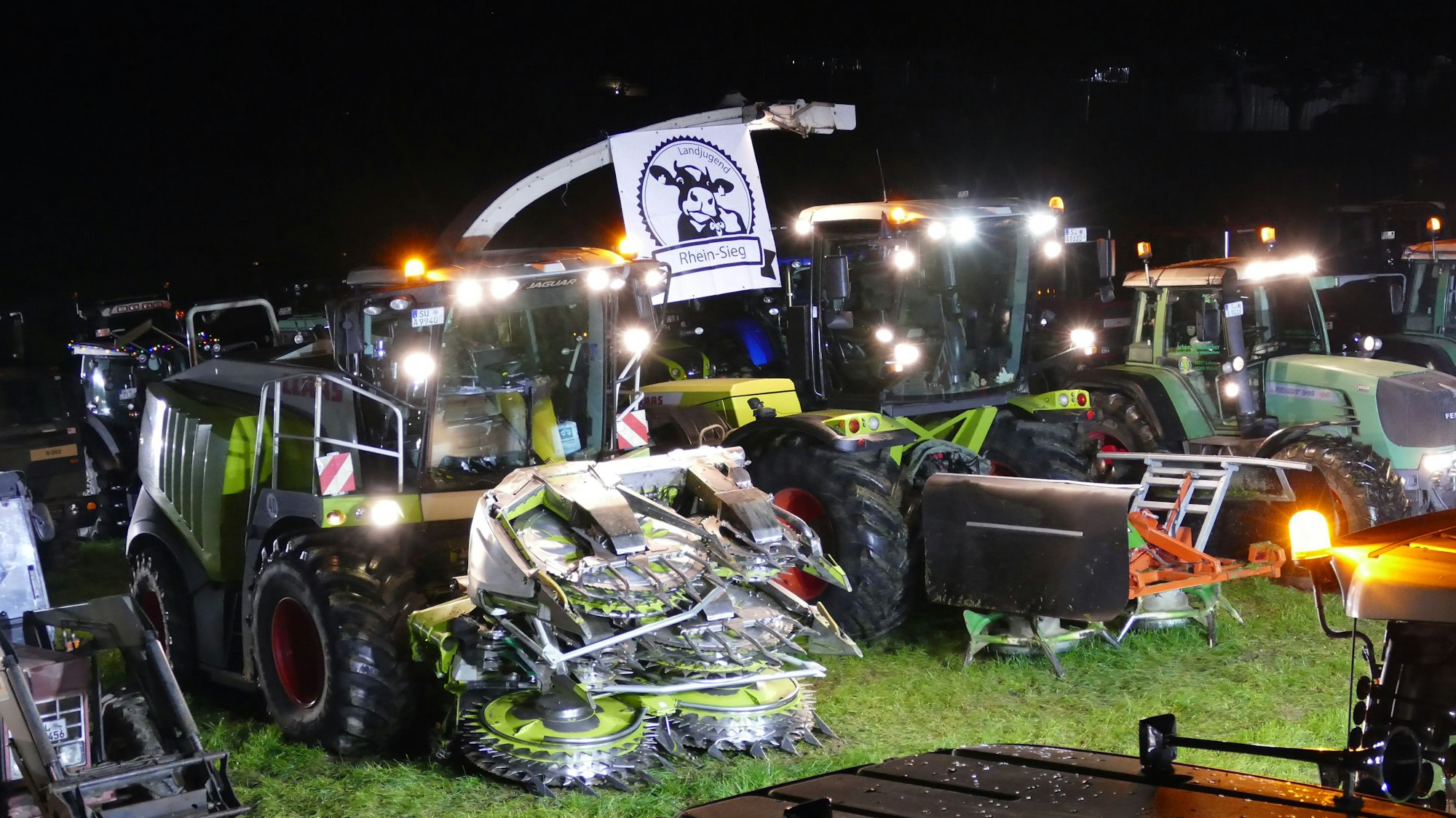 Maishäcksler und Traktoren stehen nachts auf einer Wiese.