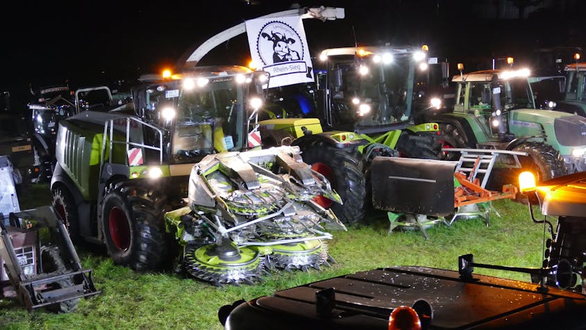 Maishäcksler und Traktoren stehen nachts auf einer Wiese.