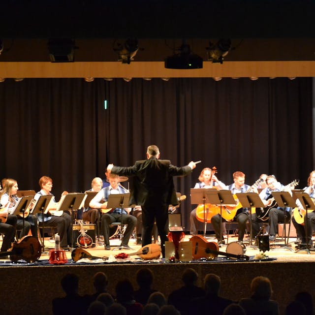 Die Musiker und Musikerinnen des Kuchenheimer Mandolinenorchesters bei einem Konzert. Der Dirigent steht mit dem Rücken zum Publikum.