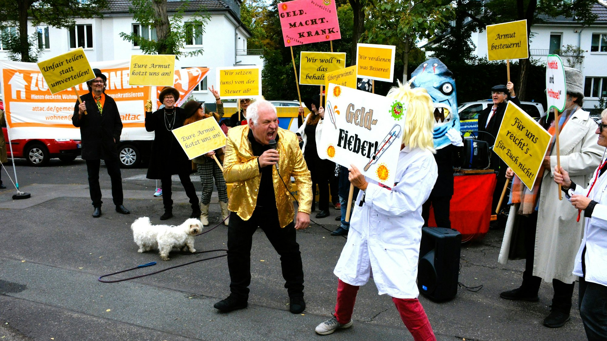 Ein Mann in einer goldfarbenen Jacke singt, während eine Frau in weißem Kittel ein Schild zeigt, auf dem „Geldfieber“ steht.