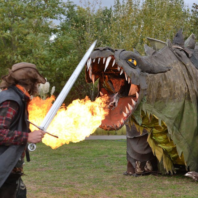 Ein Schwertkämpfer nähert sich der Figur eines feuerspeienden Drachen.