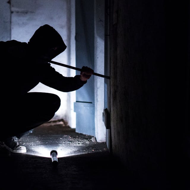 Ein Mann hebelt mit einem Brecheisen eine Tür im Keller eines Wohnhauses auf (gestellte Szene).