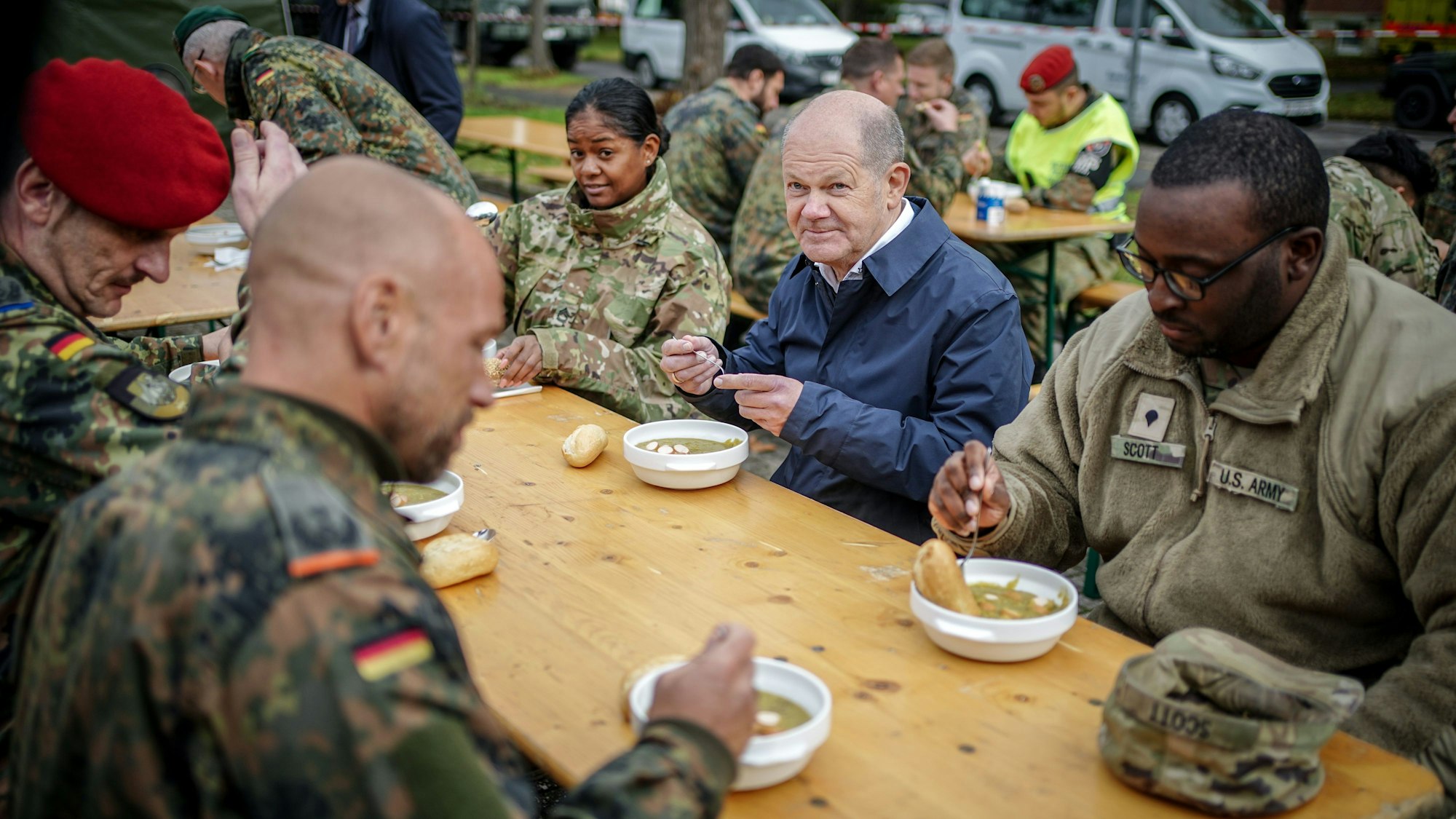 Bundeskanzler Olaf Scholz (SPD) sitzt am Rande der Fähigkeitsdemonstration der Territorialen Verfügungsgruppe auf dem Militärflughafen Köln-Wahn mit US-amerikanischen und deutschen Soldaten beim Mittagessen zusammen.
