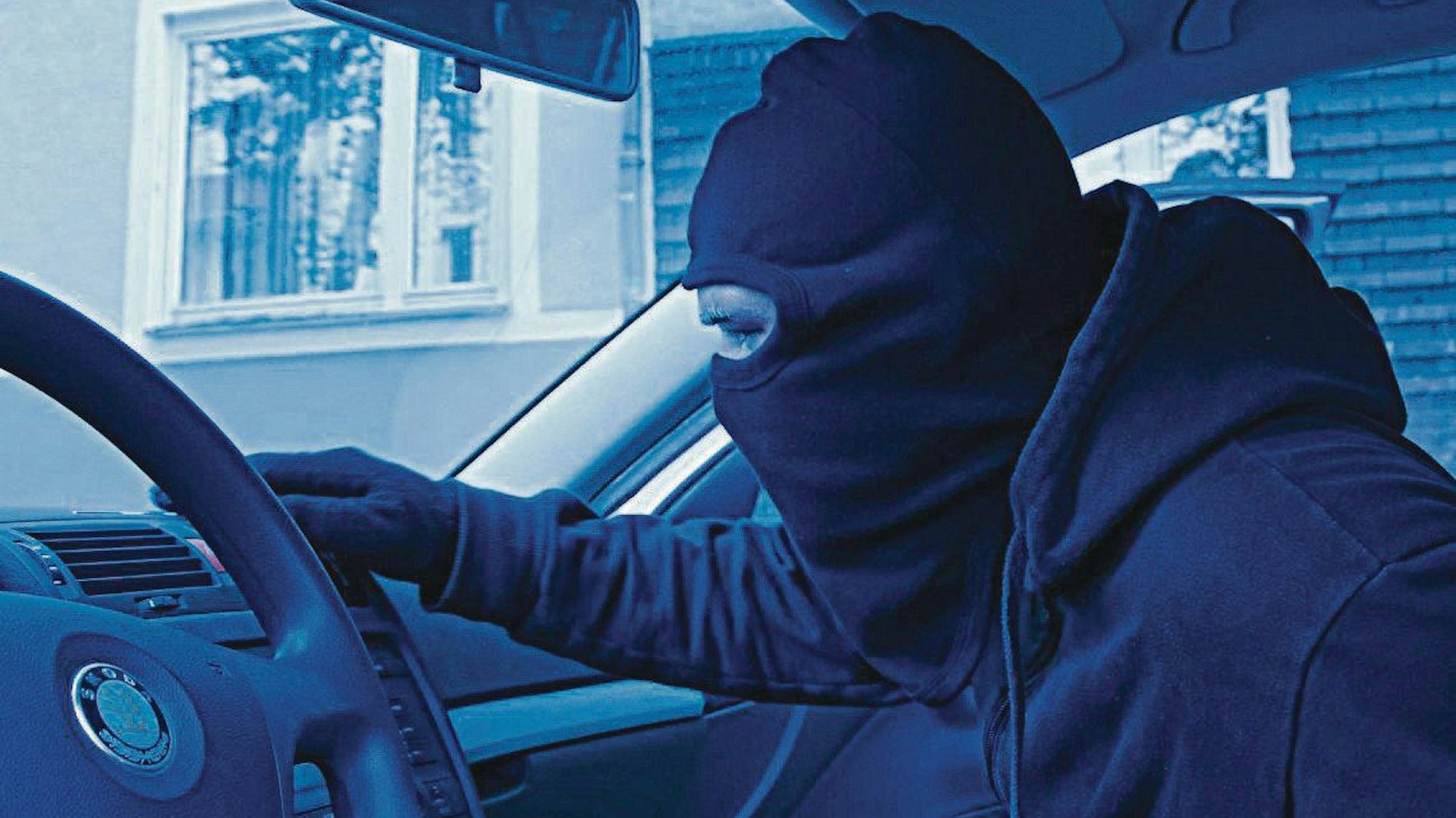 Das Bild zeigt einen maskierten Mann in einem Auto.