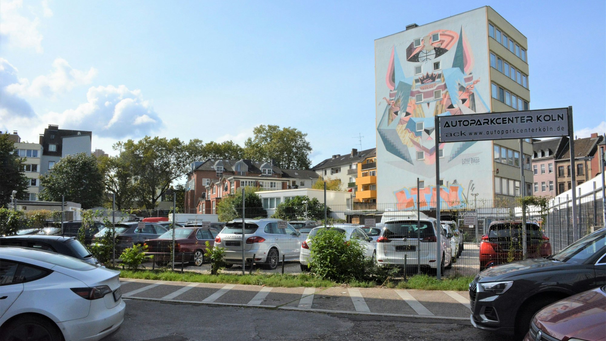 Autos stehen auf einem Parkplatz vor einem Hochhaus mit einem großen Wandgemälde.