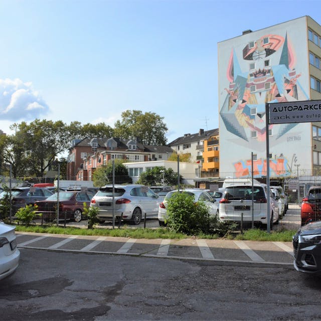 Autos stehen auf einem Parkplatz vor einem Hochhaus mit einem großen Wandgemälde.&nbsp;