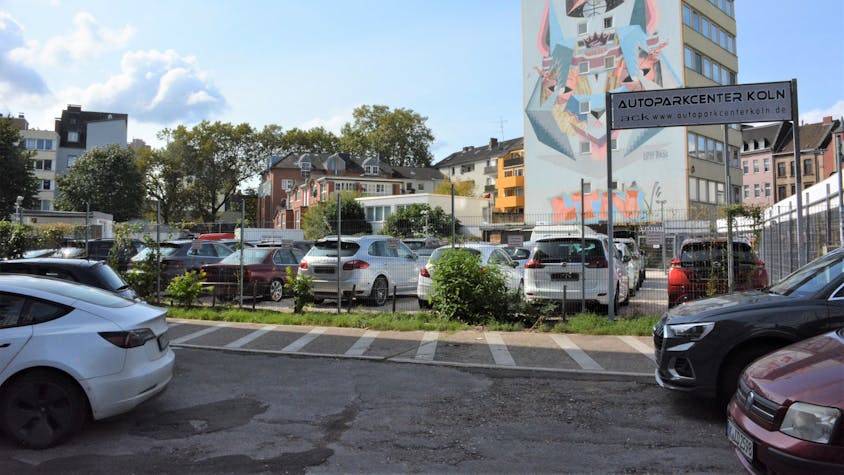 Autos stehen auf einem Parkplatz vor einem Hochhaus mit einem großen Wandgemälde.&nbsp;