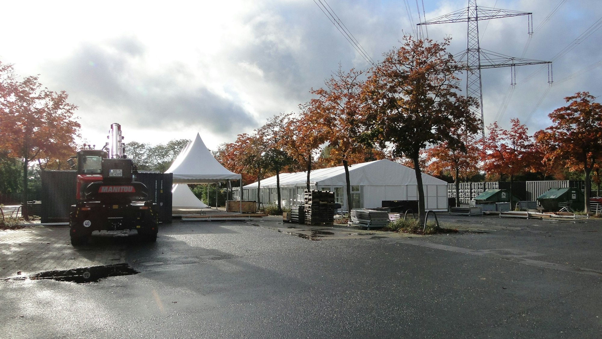 Auf einem Parkplatz mit Bäumen sind große weiße Zelte aufgebaut.