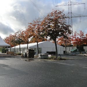 Auf einem Parkplatz mit Bäumen sind große weiße Zelte aufgebaut.
