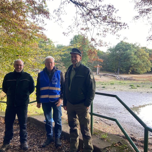 Drei Männer stehen vor dem Teich.