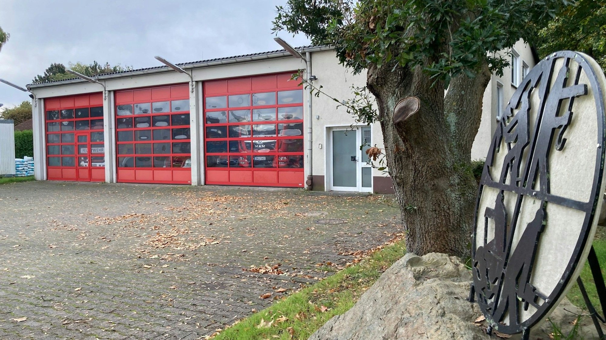 Das Feuerwehrgerätehaus in Habbelrath ist von außen zu sehen, rechts das Logo der Feuerwehr, daneben ein Baum.