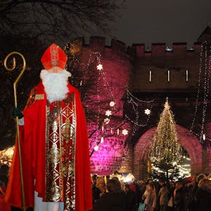 Ein Nikolaus in vollem Ornat steht vor der Kulisse der festlich geschmückten Torburg, ein Weihnachtsmarkt steht unter dem Torbogen.