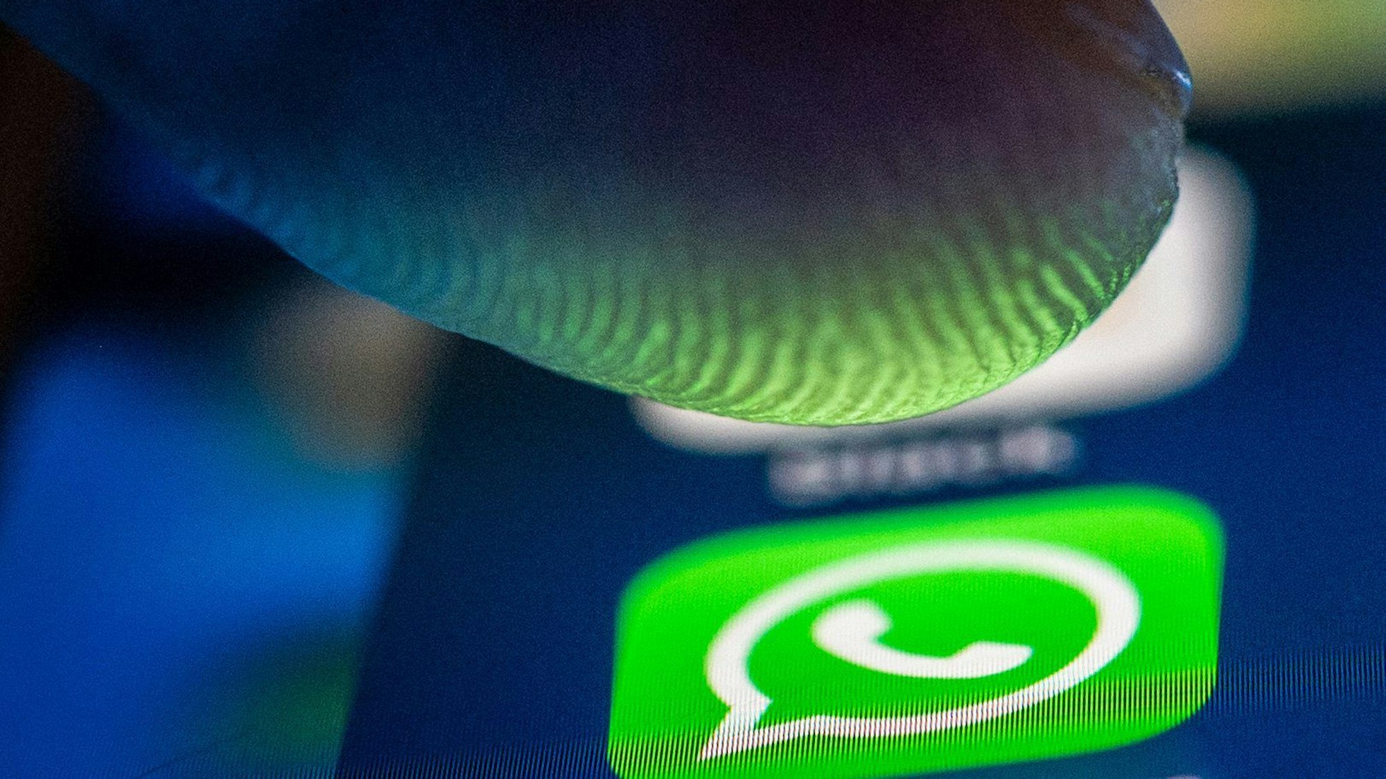 Ein Finger nähert sich dem Whatsapp-Logo auf einem Smartphone.